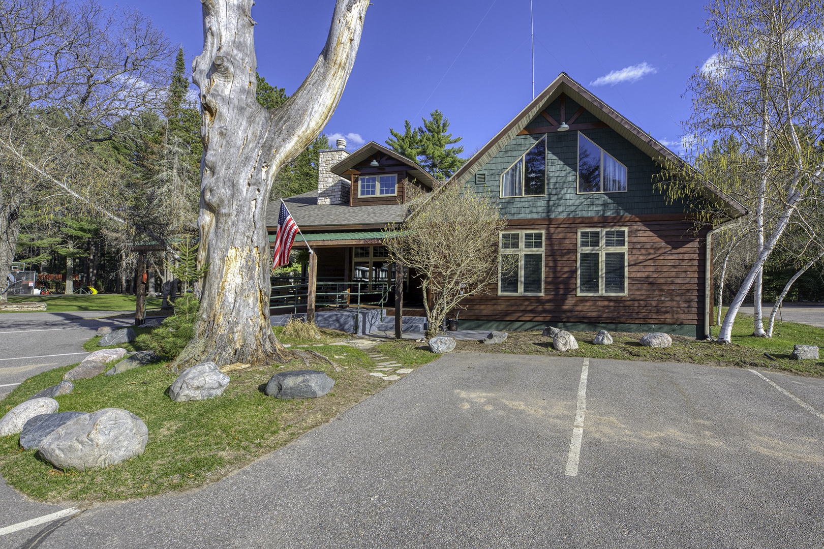 This charming property features a welcoming exterior with rustic wood siding, spacious front lawn with mature trees, and dedicated parking spaces for convenient arrivals.