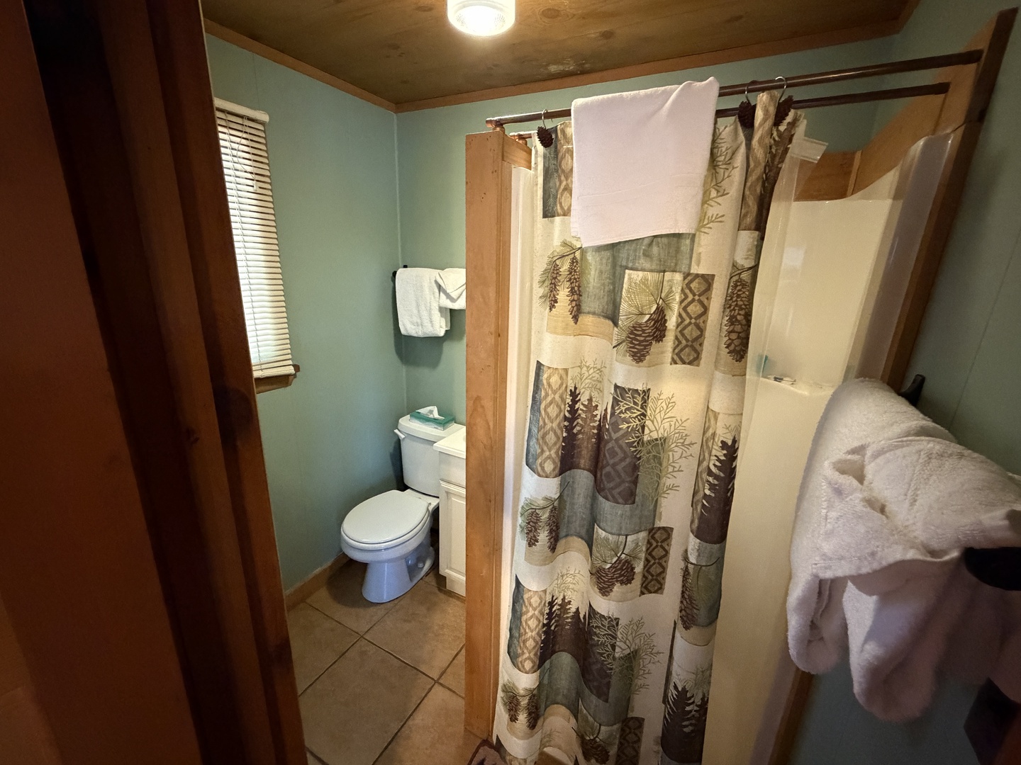 Step into your private bathroom with rustic charm, featuring a pine-inspired shower curtain and warm wood accents that bring a cozy, cabin-like feel to your stay.