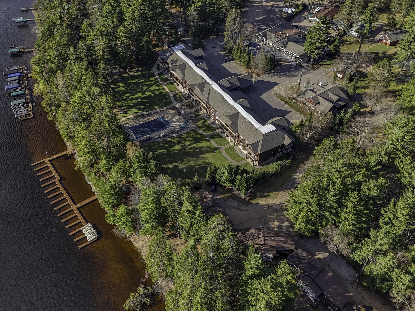 An aerial view showcasing the waterfront property nestled among tall pines, with docks extending into the lake and spacious grounds surrounded by natural forest scenery.