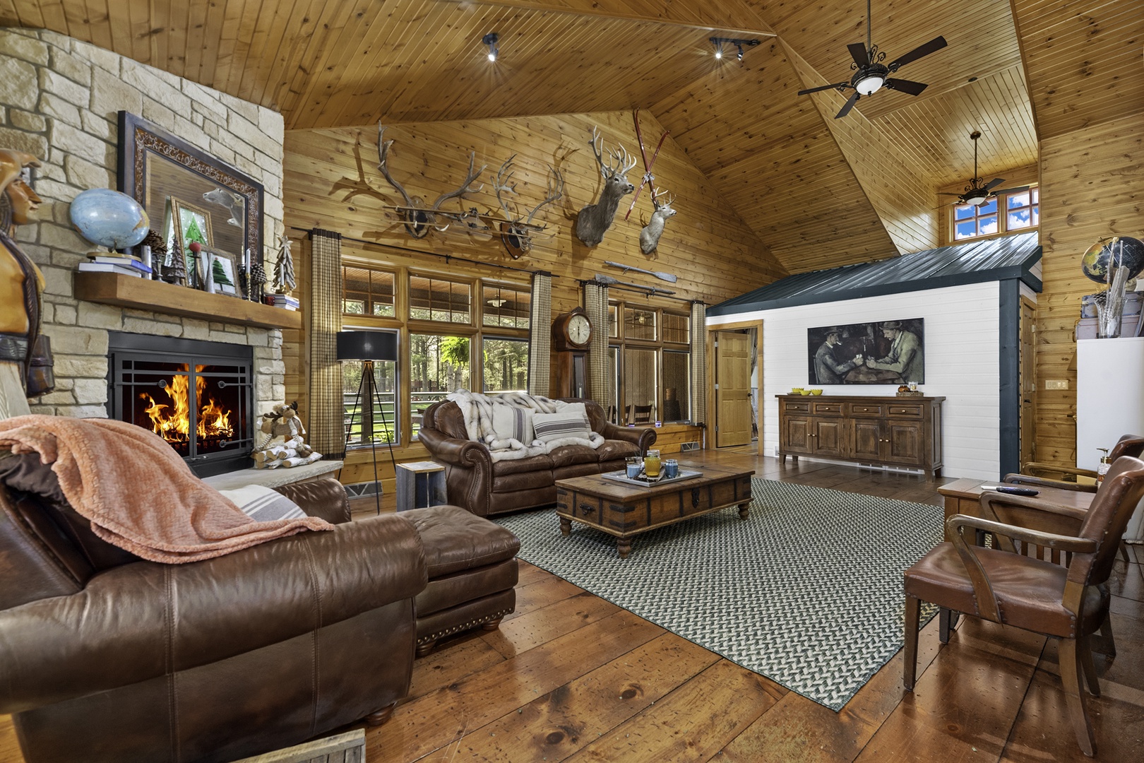 Gather around the crackling fireplace in this spacious great room, where vaulted wood ceilings, rustic leather seating, and natural light create a warm retreat after your day's adventures.