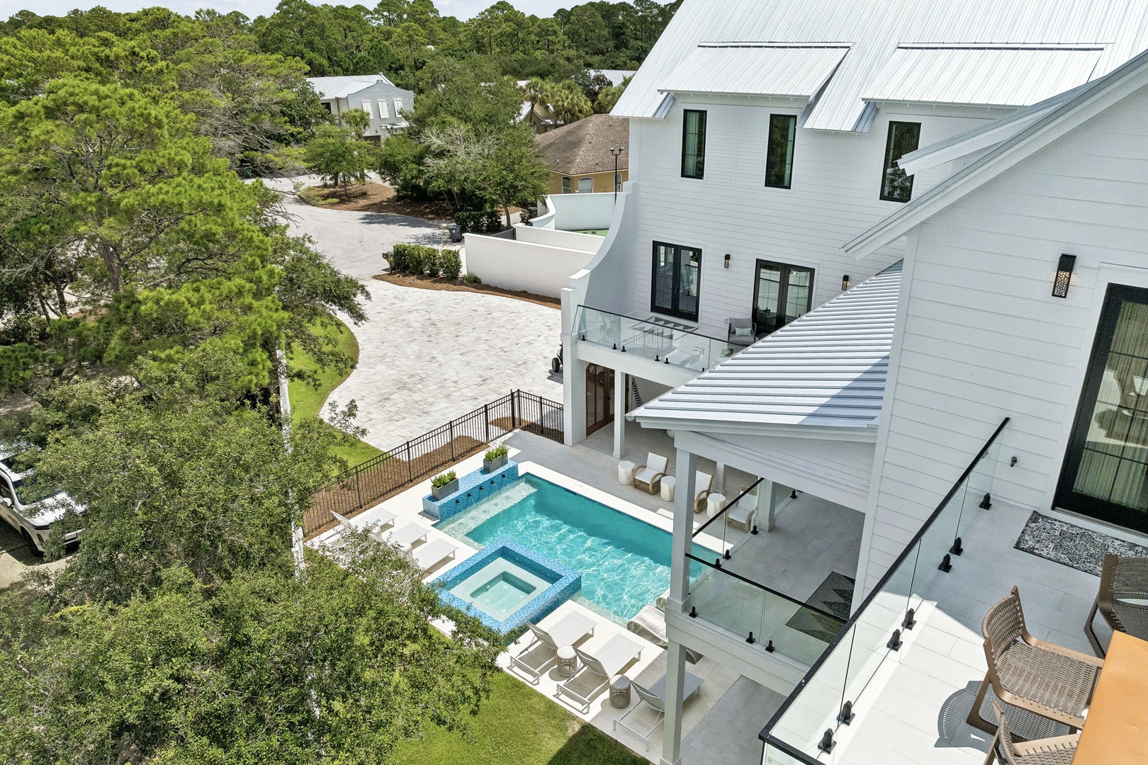 Stunning modern white coastal home with private pool, hot tub, and multiple outdoor lounging areas nestled within a lush, tree-lined neighborhood.