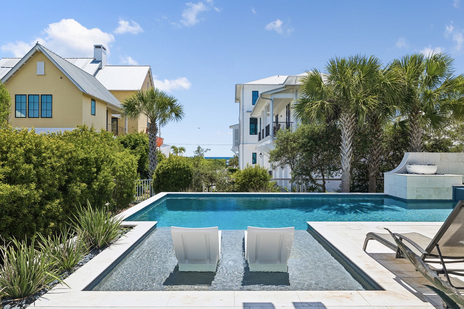 Luxurious pool with integrated tanning ledge and loungers, surrounded by lush tropical landscaping. A peaceful coastal retreat with elegant modern design, just steps from the beach.