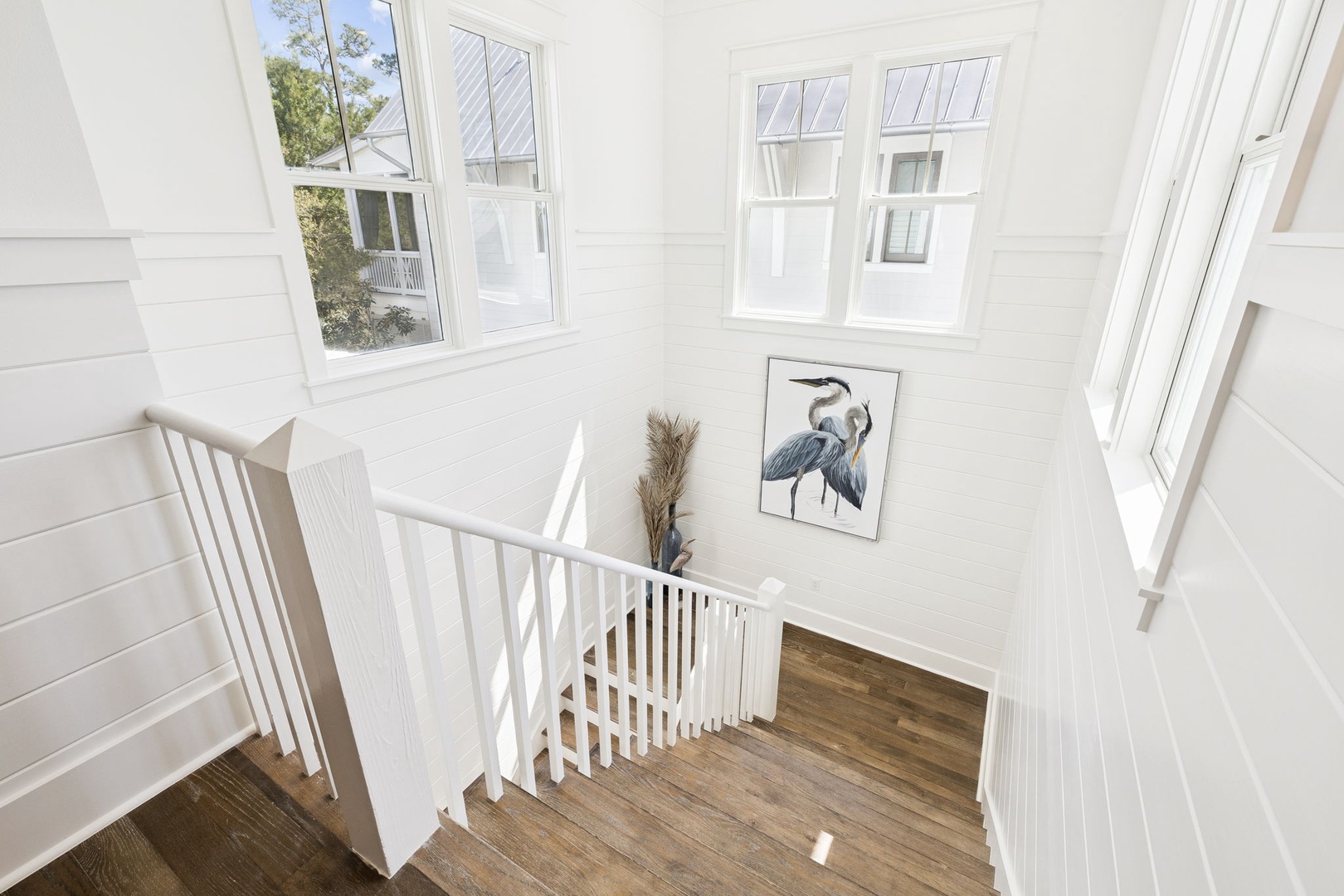 Sunlight streams through soaring windows in this bright, elegant stairway where coastal artwork adds character to your peaceful retreat.