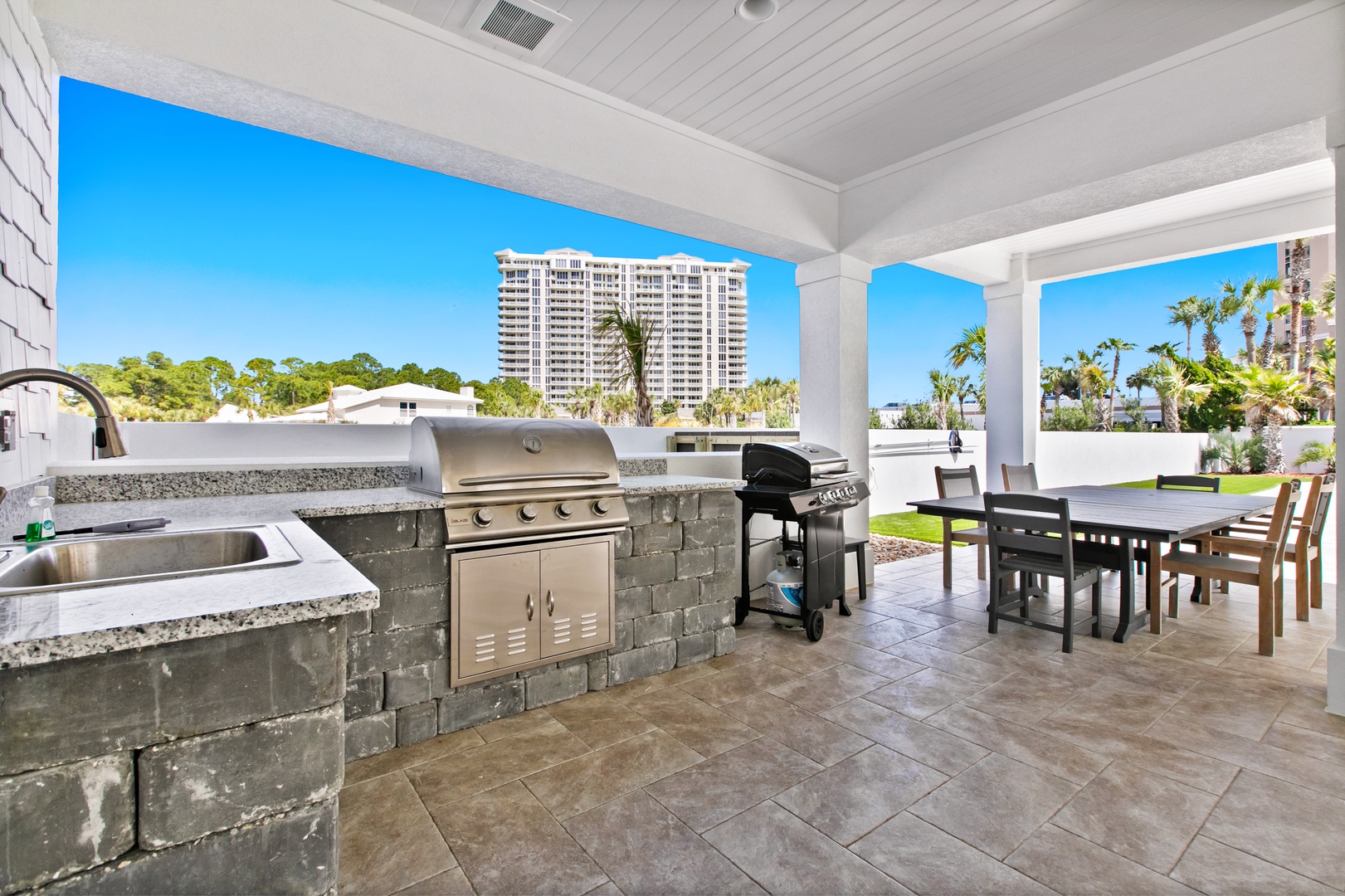 Picture yourself grilling up a feast on your private covered patio, complete with a full outdoor kitchen, sink, and spacious dining area—perfect for sunny afternoons with tropical breezes and lush palm trees all around.