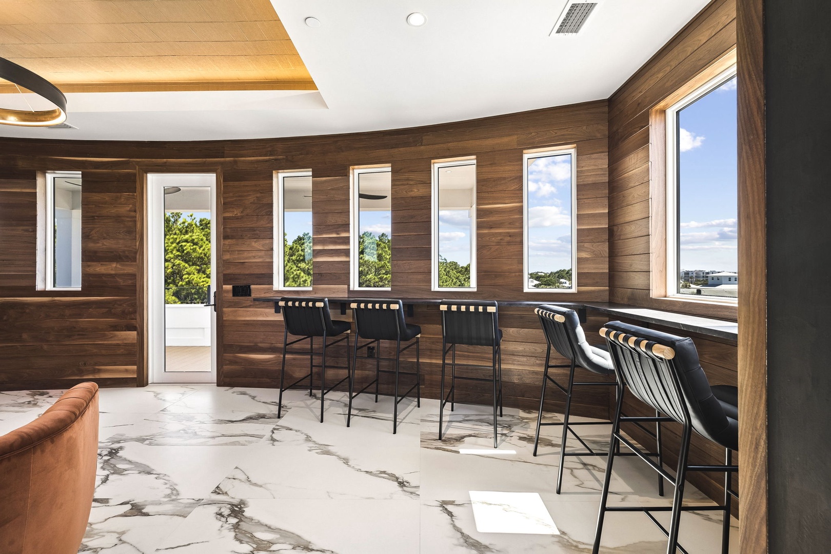 Gather around the sleek bar with friends and enjoy open views through expansive windows, where natural light streams across elegant marble floors and warm wood walls.