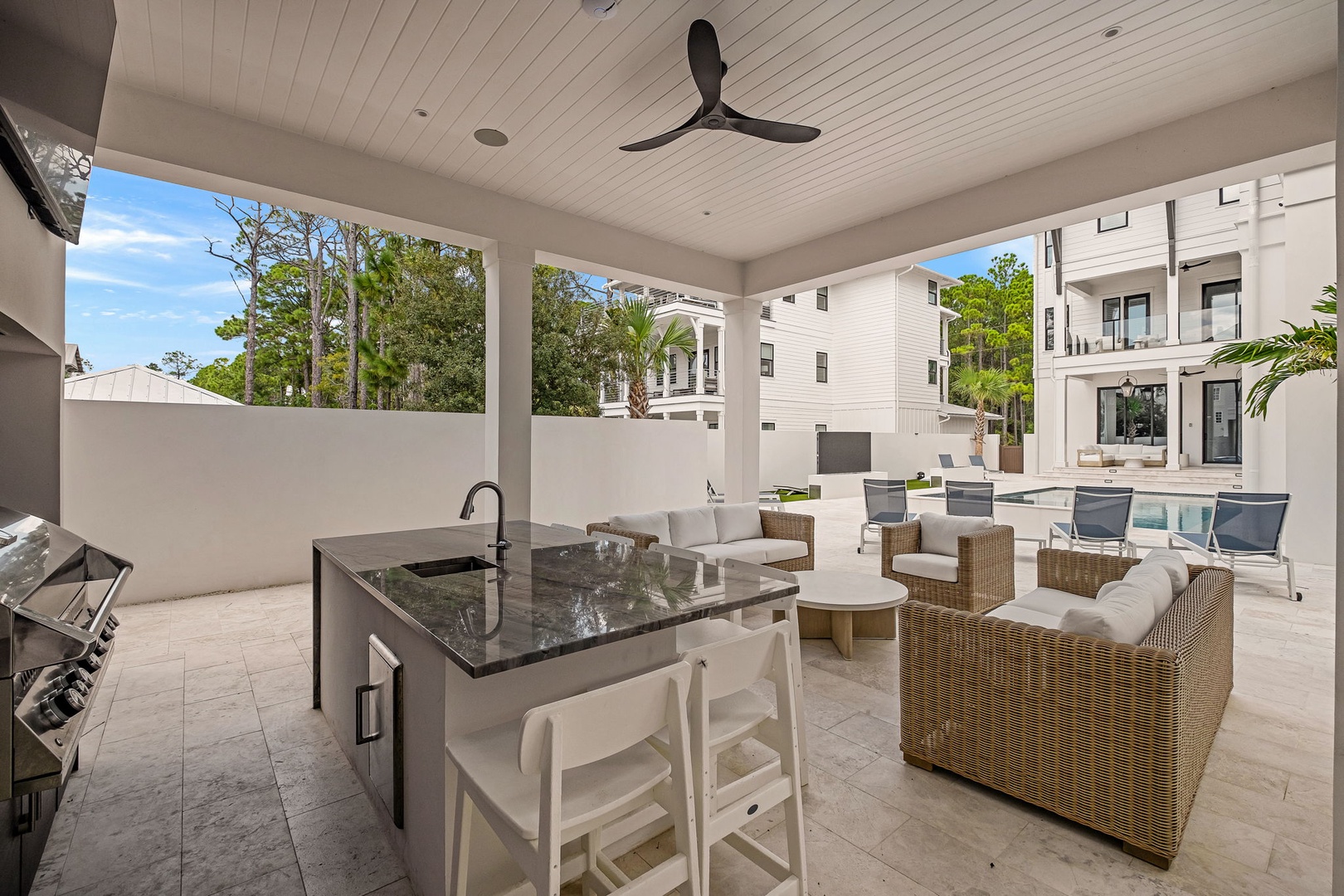 Your private outdoor kitchen opens to a breezy covered patio with elegant lounge seating overlooking the sparkling pool—perfect for seamless entertaining and relaxed indoor-outdoor living.