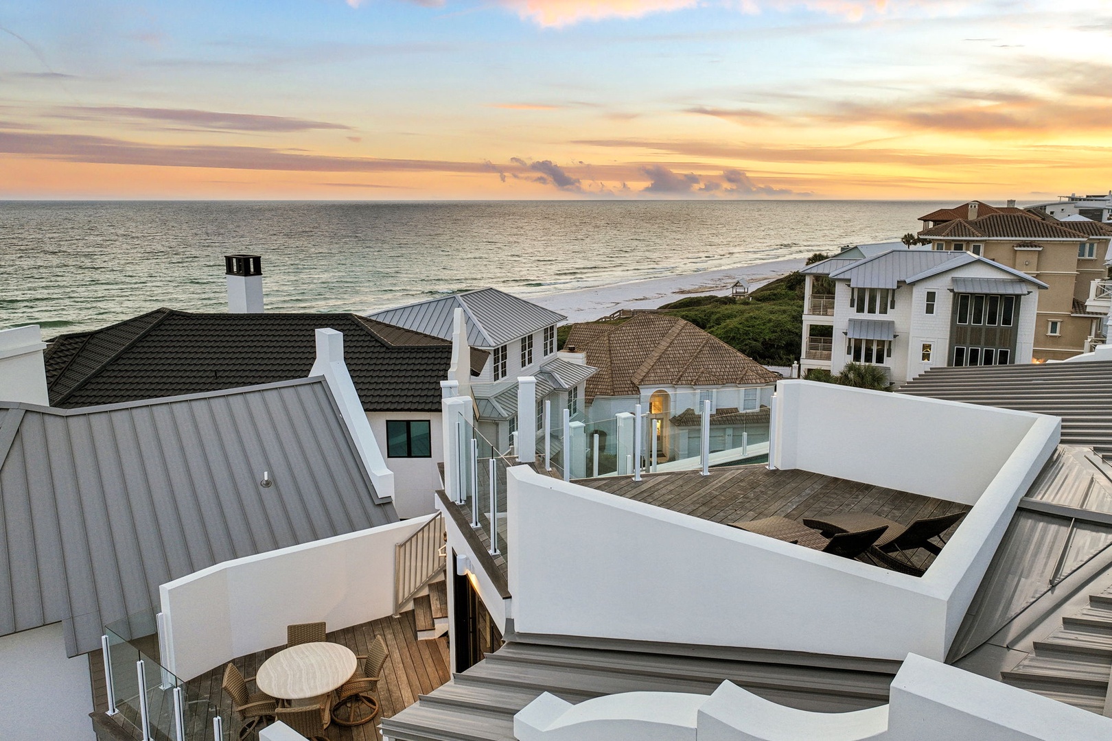 Elevated beachfront property overlooking serene coastal waters, featuring modern architecture with multiple rooftop terraces, situated in a quiet residential neighborhood with direct beach access.