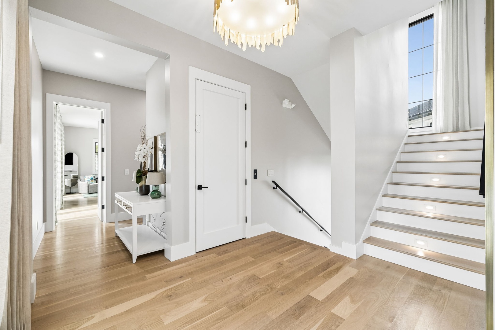 Step into your bright, elegantly lit entryway featuring warm hardwood floors, modern staircase, and airy hallways that welcome you home with style and comfort.