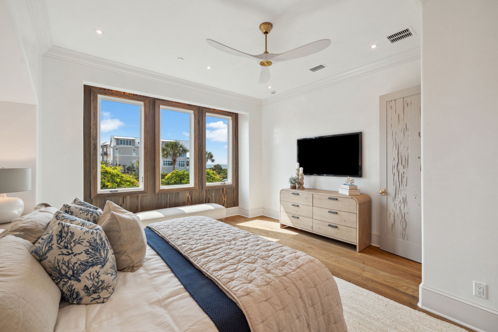 Wake up to natural light streaming through expansive windows framing lush coastal views. Your peaceful bedroom features warm wood floors, a plush king bed, ceiling fan for comfort, and modern entertainment—your perfect retreat after sun-soaked days.