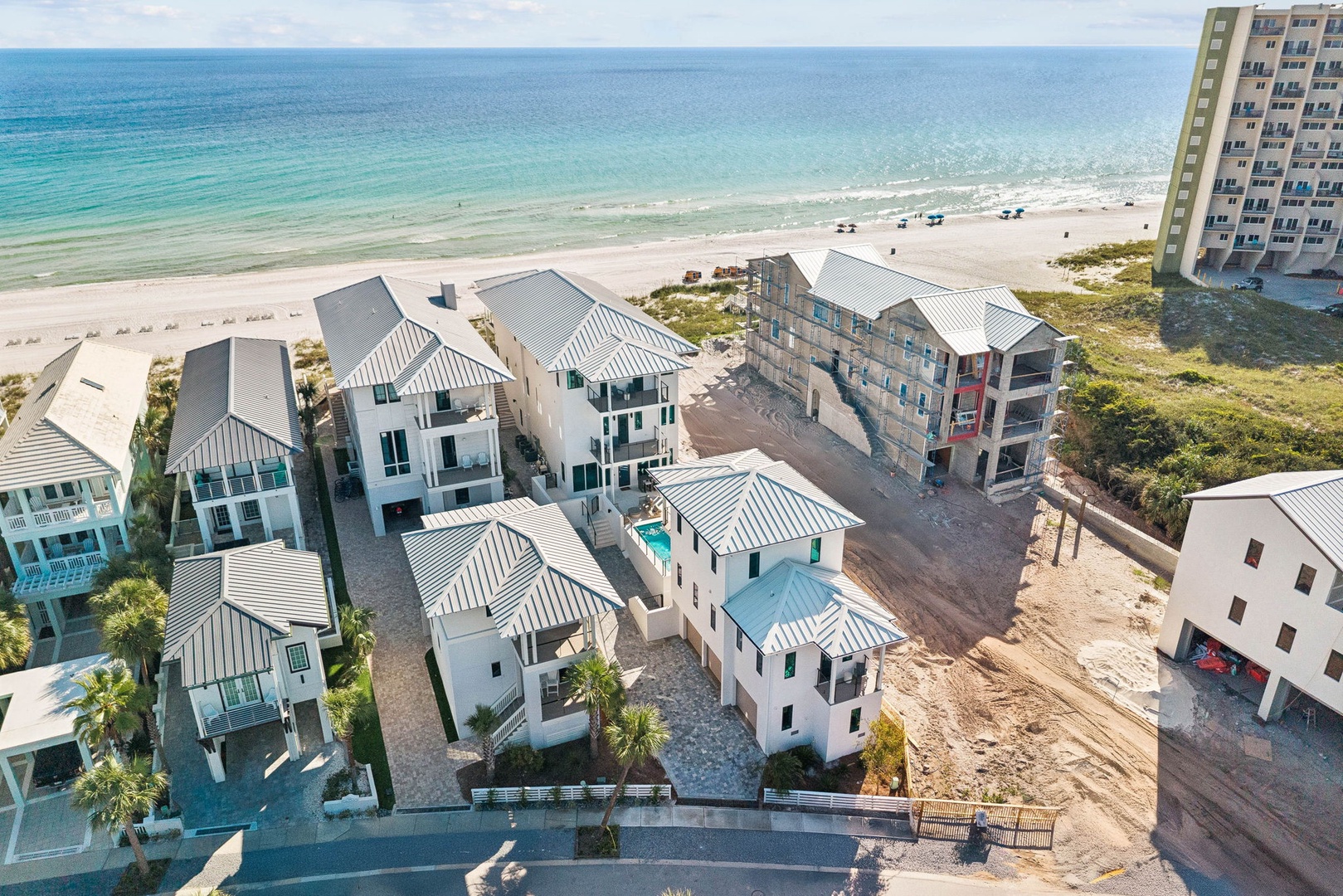 An aerial view showcasing beachfront vacation homes with white roofs nestled between the turquoise Gulf waters and pristine white sand, offering a peaceful coastal getaway setting.