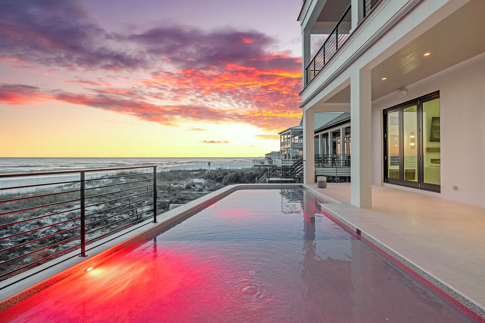 Stunning beachfront property featuring modern architecture with oceanside pool and dramatic sunset views over pristine coastline.