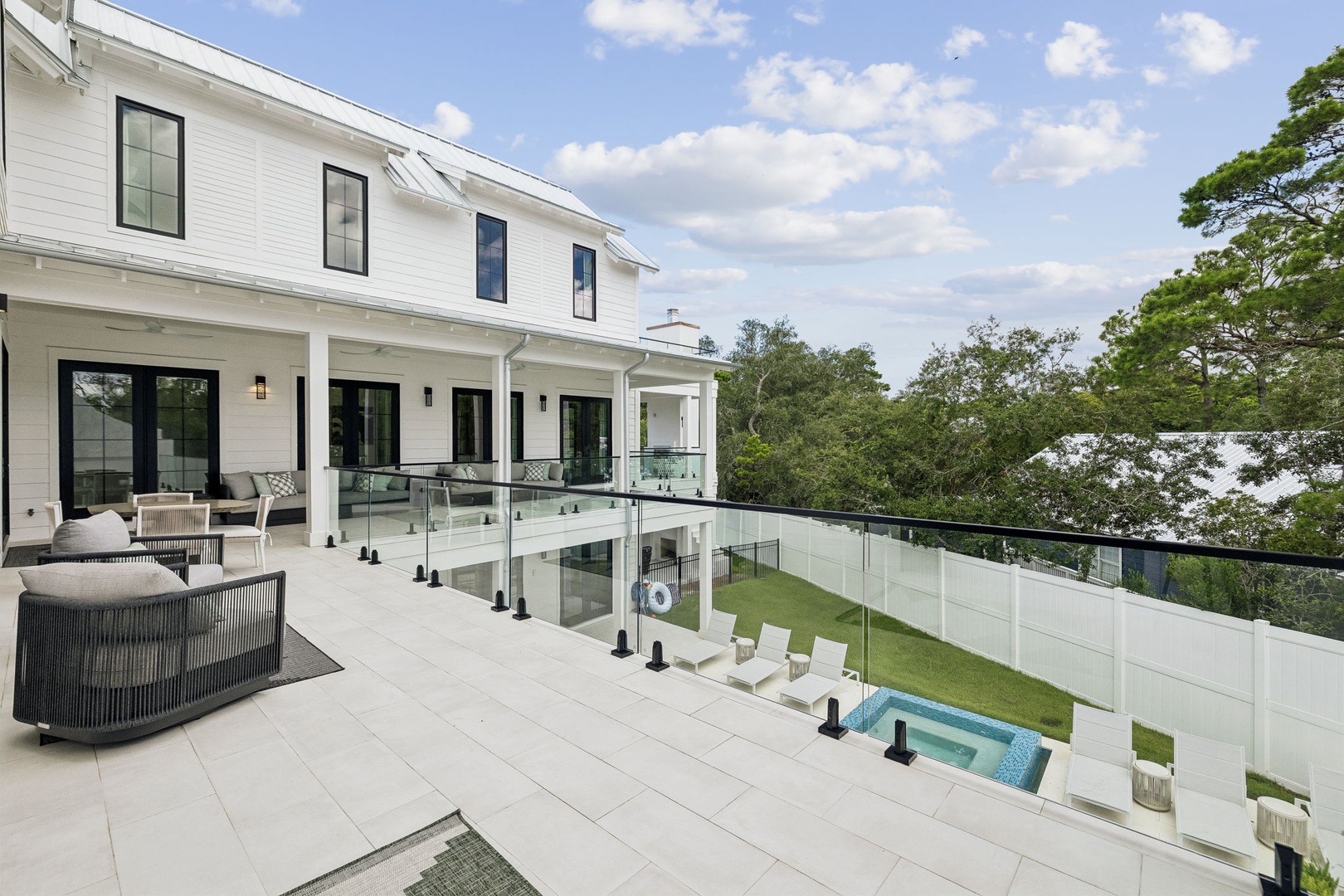 A stunning white modern farmhouse with expansive outdoor terrace and lush treetop views framed by a glass-paneled railing.