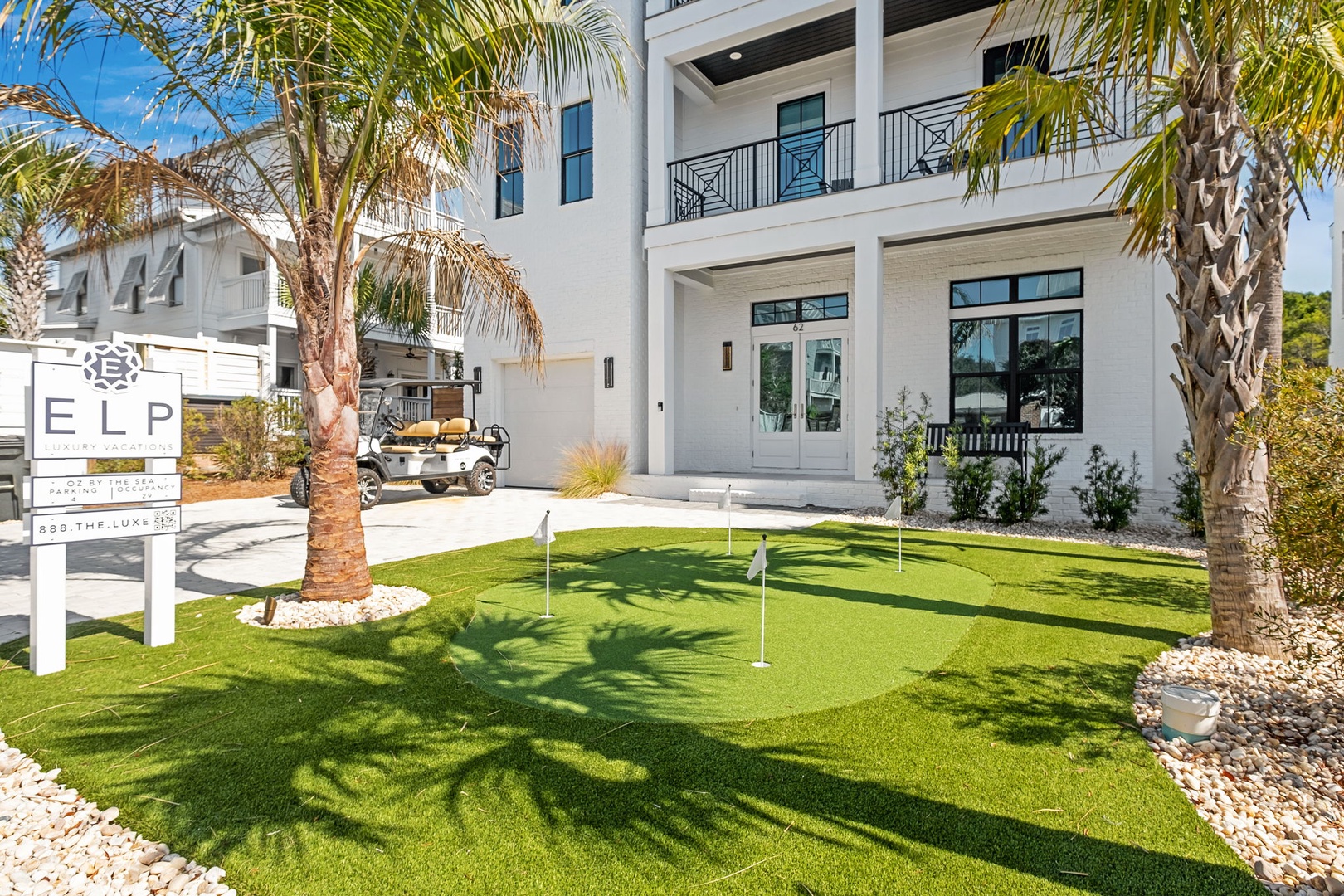 Modern beachfront property featuring a private putting green surrounded by tropical palms and coastal landscaping.