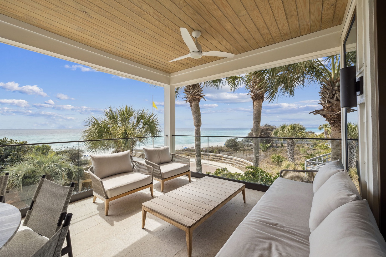 Relax on your private terrace with plush seating and breathtaking ocean views through swaying palms—your perfect coastal retreat awaits.