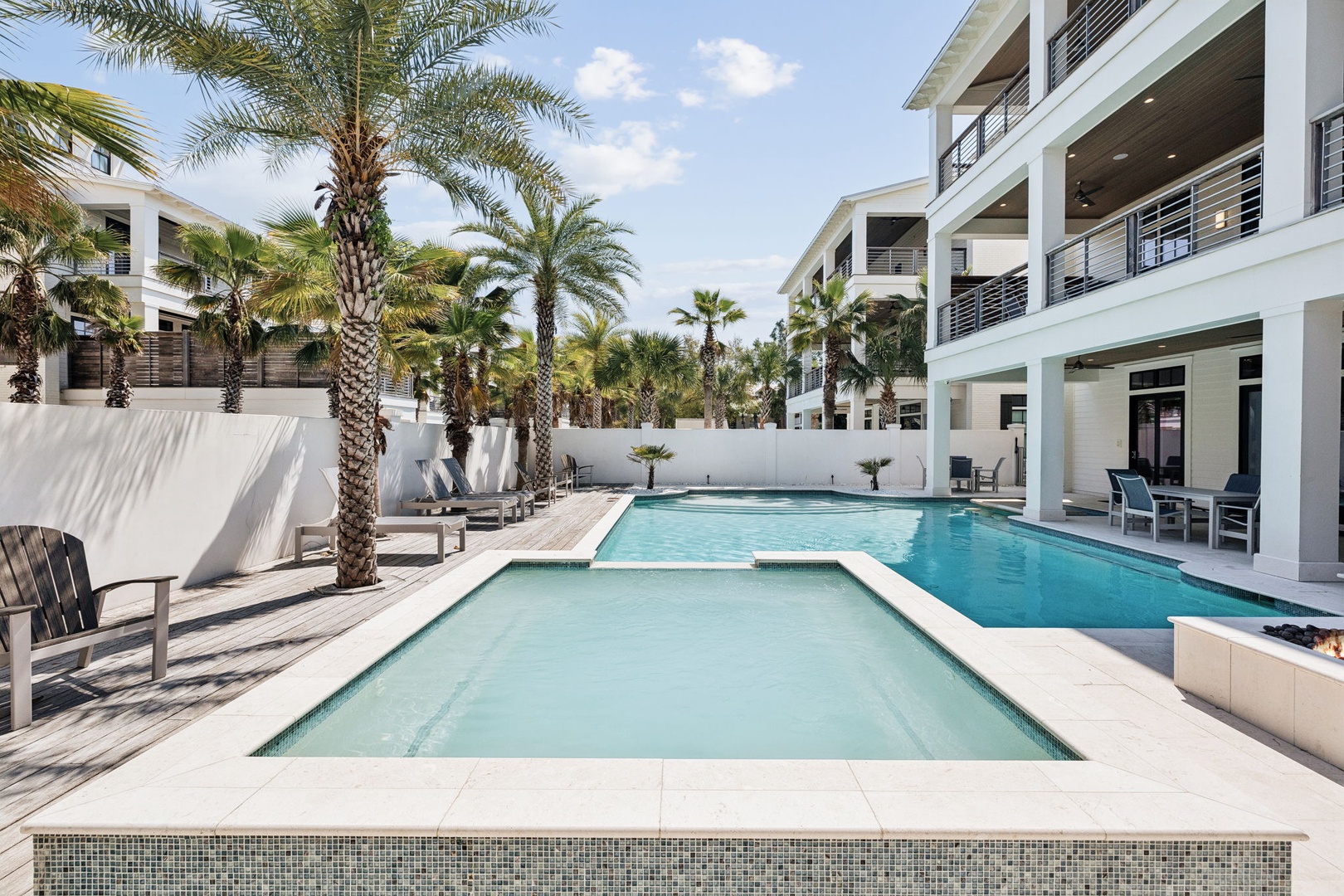 Modern multi-level property featuring dual swimming pools surrounded by tropical palm trees and contemporary architecture in a resort-style setting.
