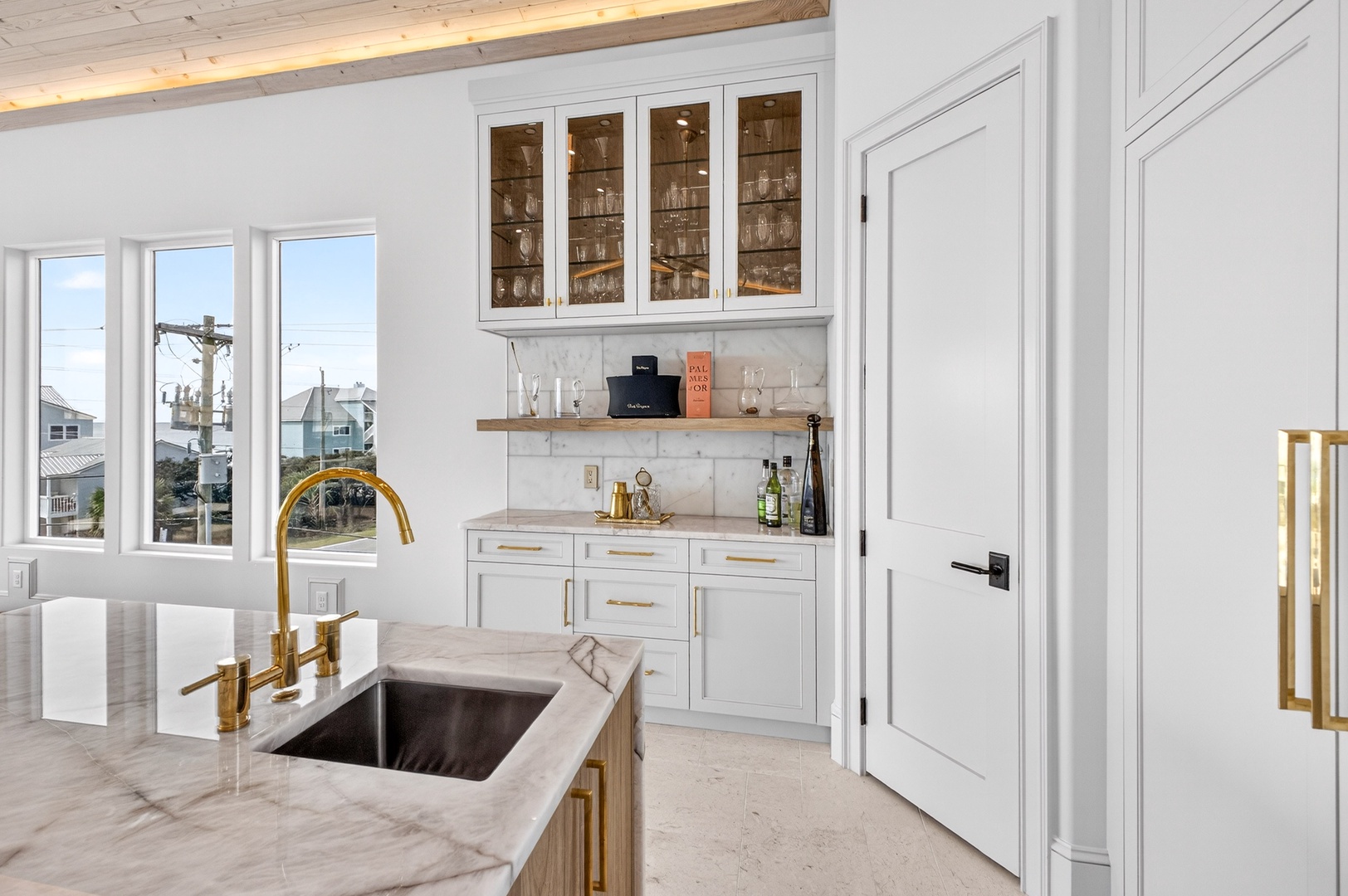 Your elegant kitchen features gleaming marble counters, gold fixtures, and stunning coastal views through every window.