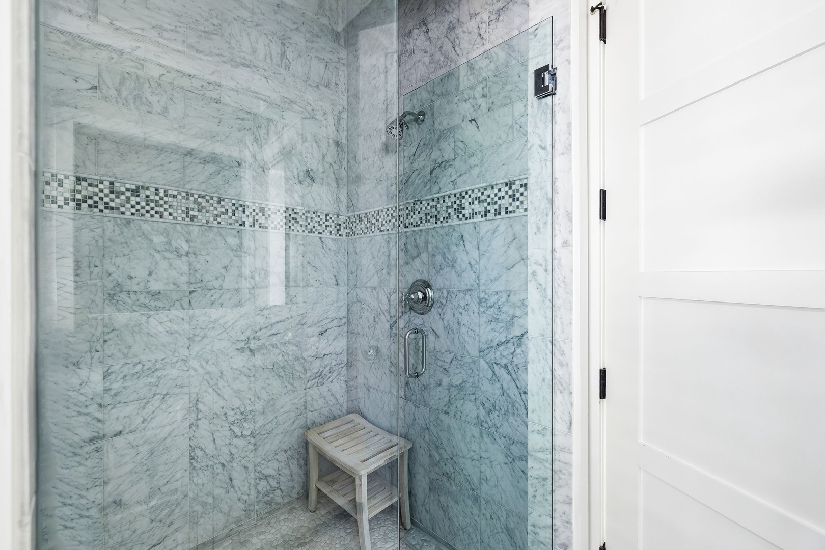 Step into your spa-like walk-in shower with elegant marble-look tile and a decorative mosaic accent that wraps the walls. A handheld showerhead and convenient teak bench make it easy to relax and refresh.