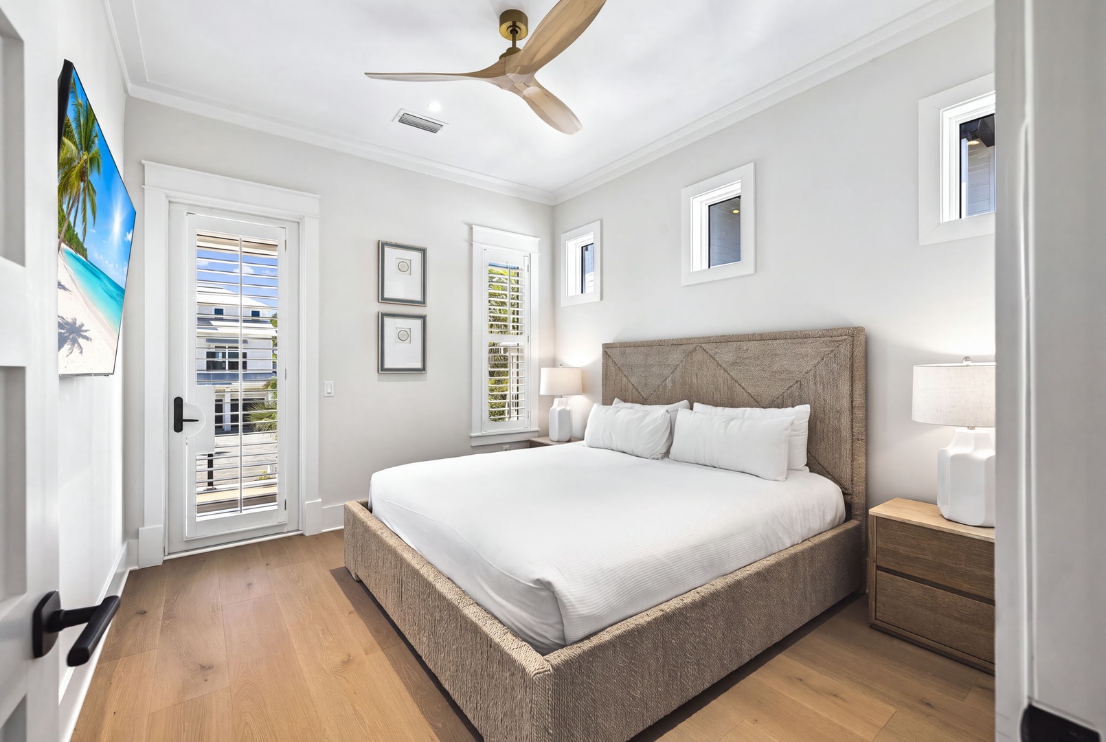 Your serene bedroom retreat features crisp linens, warm wood tones, and a ceiling fan for comfort, with natural light streaming through plantation shutters and balcony access just steps away.