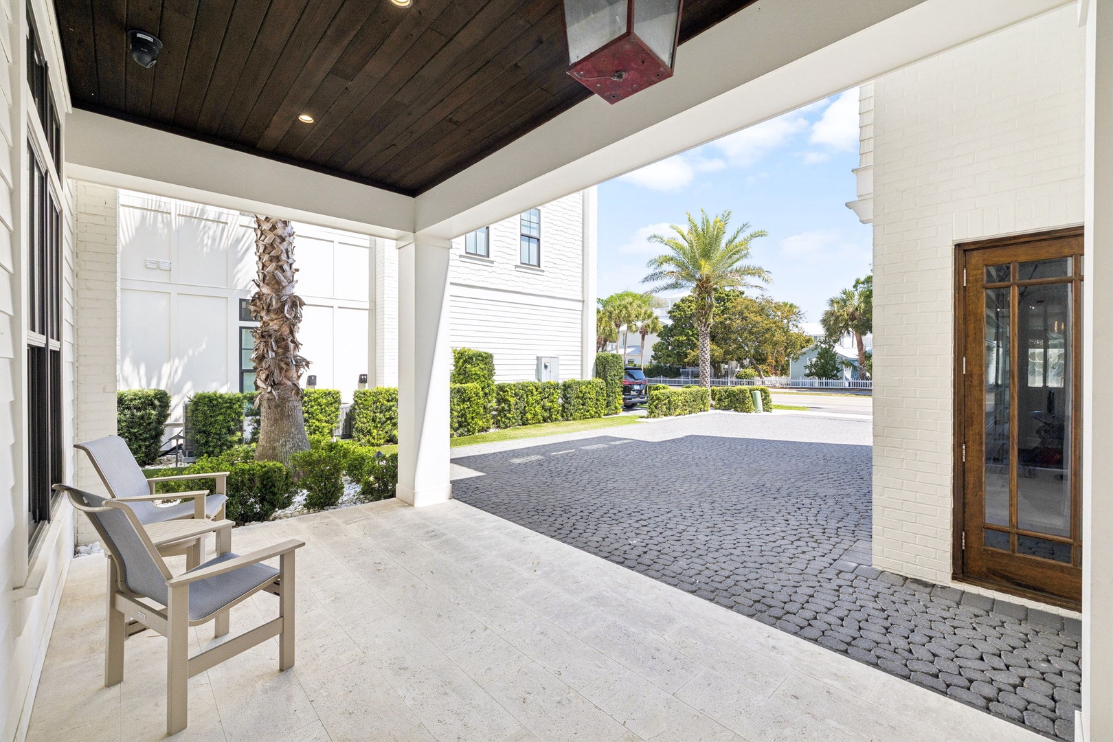 A covered porch with seating overlooking a charming cobblestone courtyard lined with palm trees and manicured hedges.
