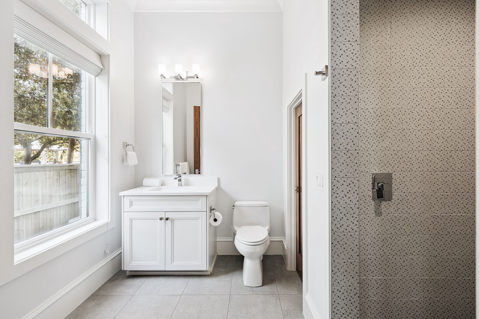 Freshen up in your bright, modern bathroom with crisp white vanity, natural light from oversized windows, and elegant patterned shower.