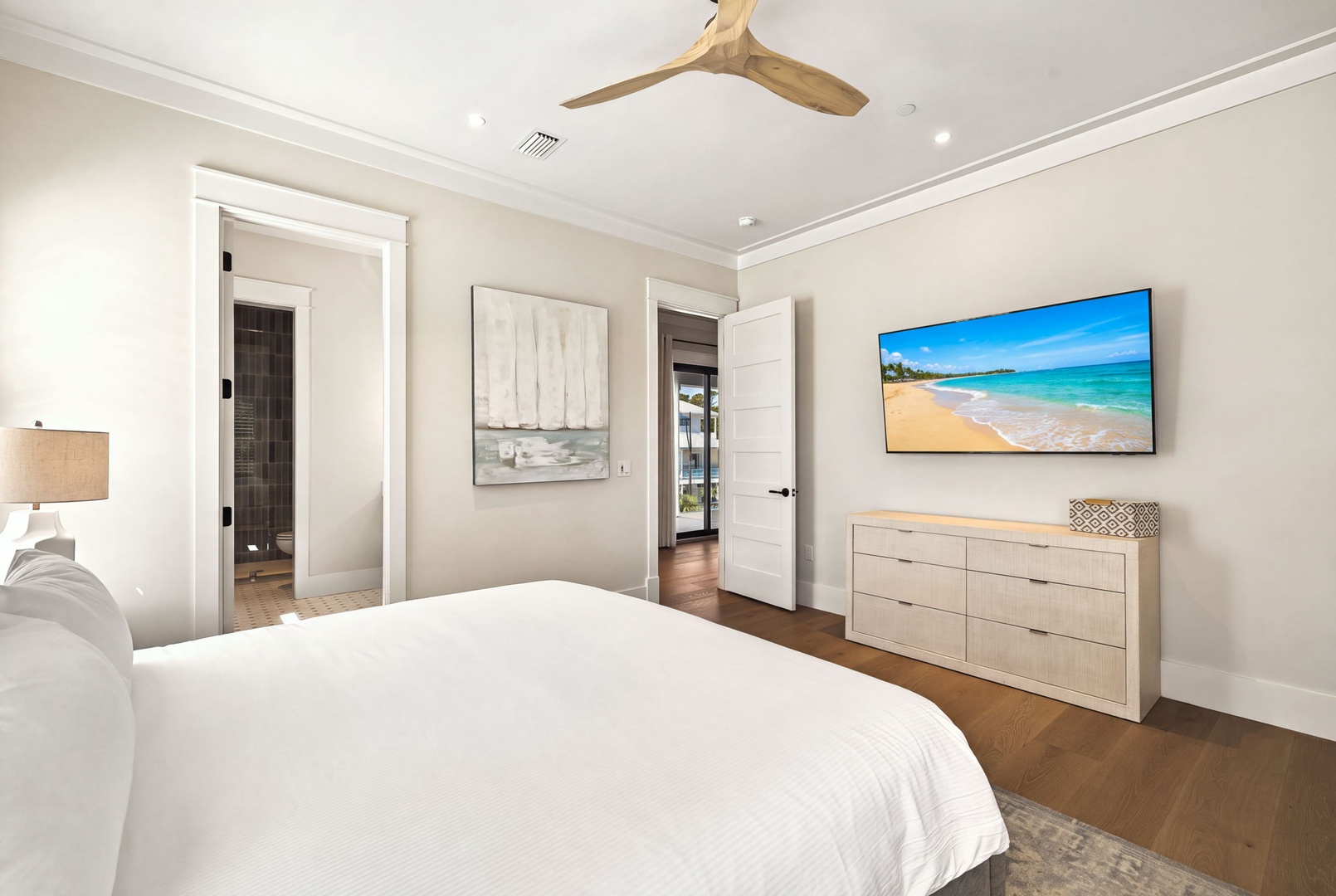 Unwind in this serene bedroom with its plush bedding and thoughtful touches. A gentle ceiling fan, soft lighting, and coastal artwork create a peaceful retreat for restful nights.