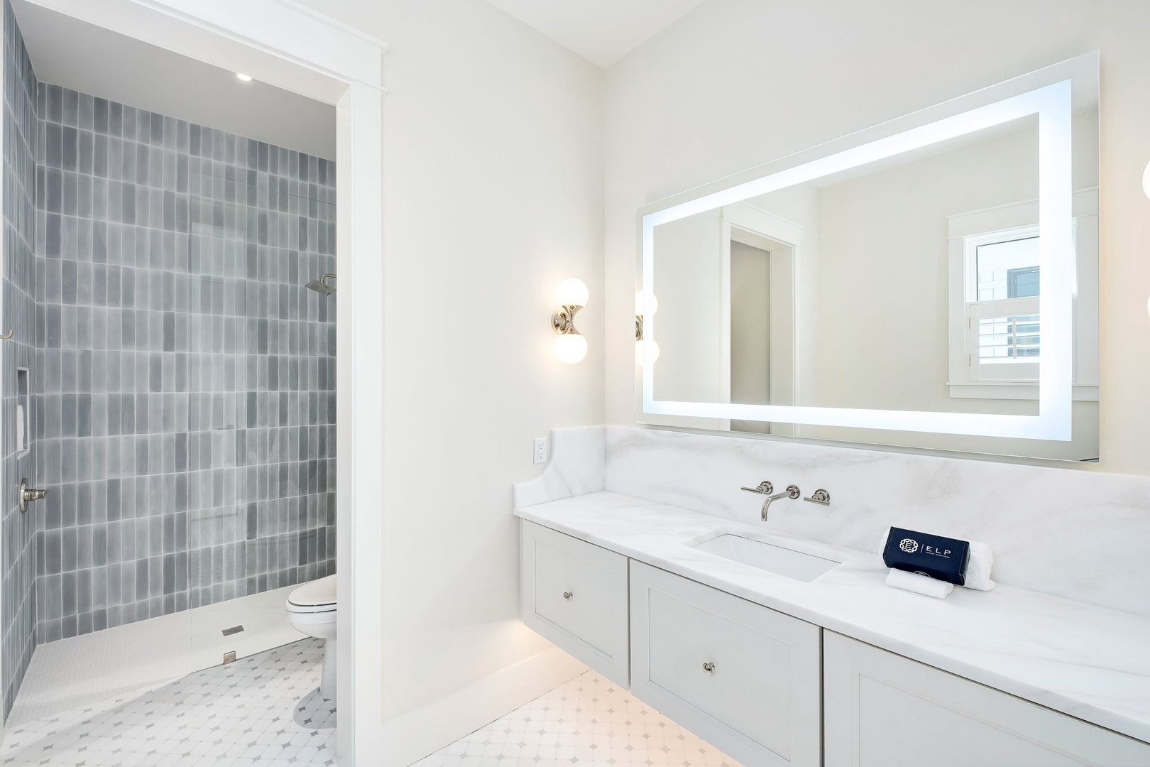 Unwind in this pristine bathroom featuring elegant tile work, a sleek vanity with marble countertops, and a spacious walk-in shower with modern gray tile.