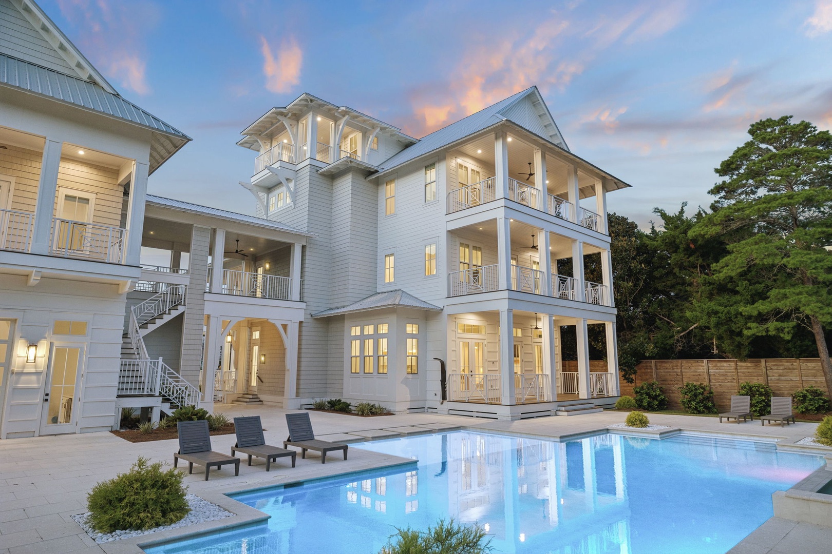 An elegant coastal retreat with multiple balconies and a sparkling pool awaits your arrival at dusk, where warm lights and sunset hues create the perfect vacation ambiance.