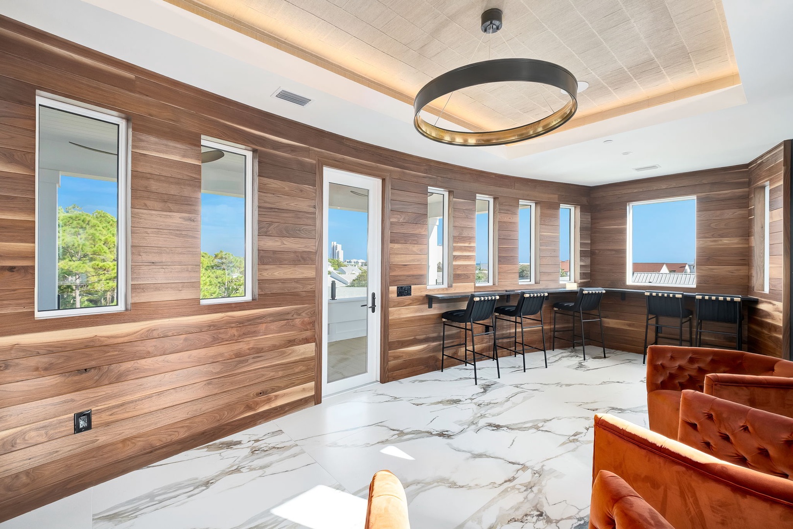 Gather with friends in this stunning lounge featuring warm wood walls, modern seating, and abundant natural light streaming through multiple windows—perfect for your morning coffee or evening conversations.