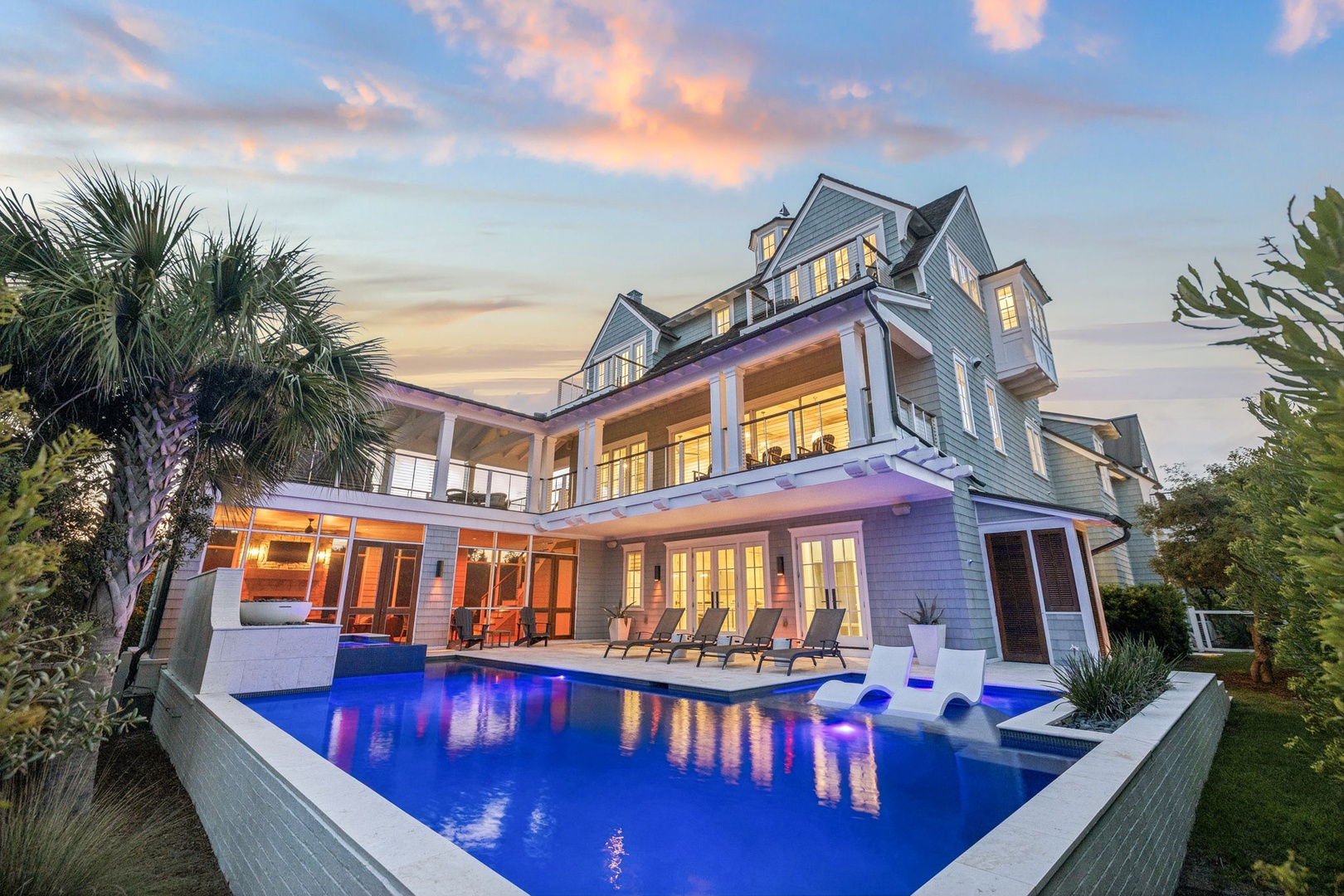 A stunning coastal estate framed by palm trees, featuring illuminated interiors and a glowing pool at twilight, set in a beautifully landscaped tropical setting.
