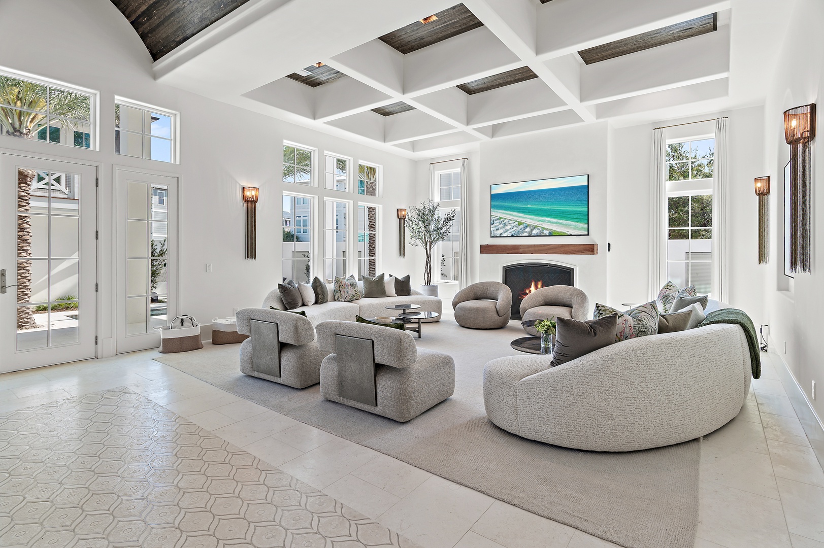 Unwind in your spacious living room, where natural light pours through expansive windows, illuminating plush seating and a striking coffered ceiling with rich wood accents. Your perfect coastal retreat awaits.
