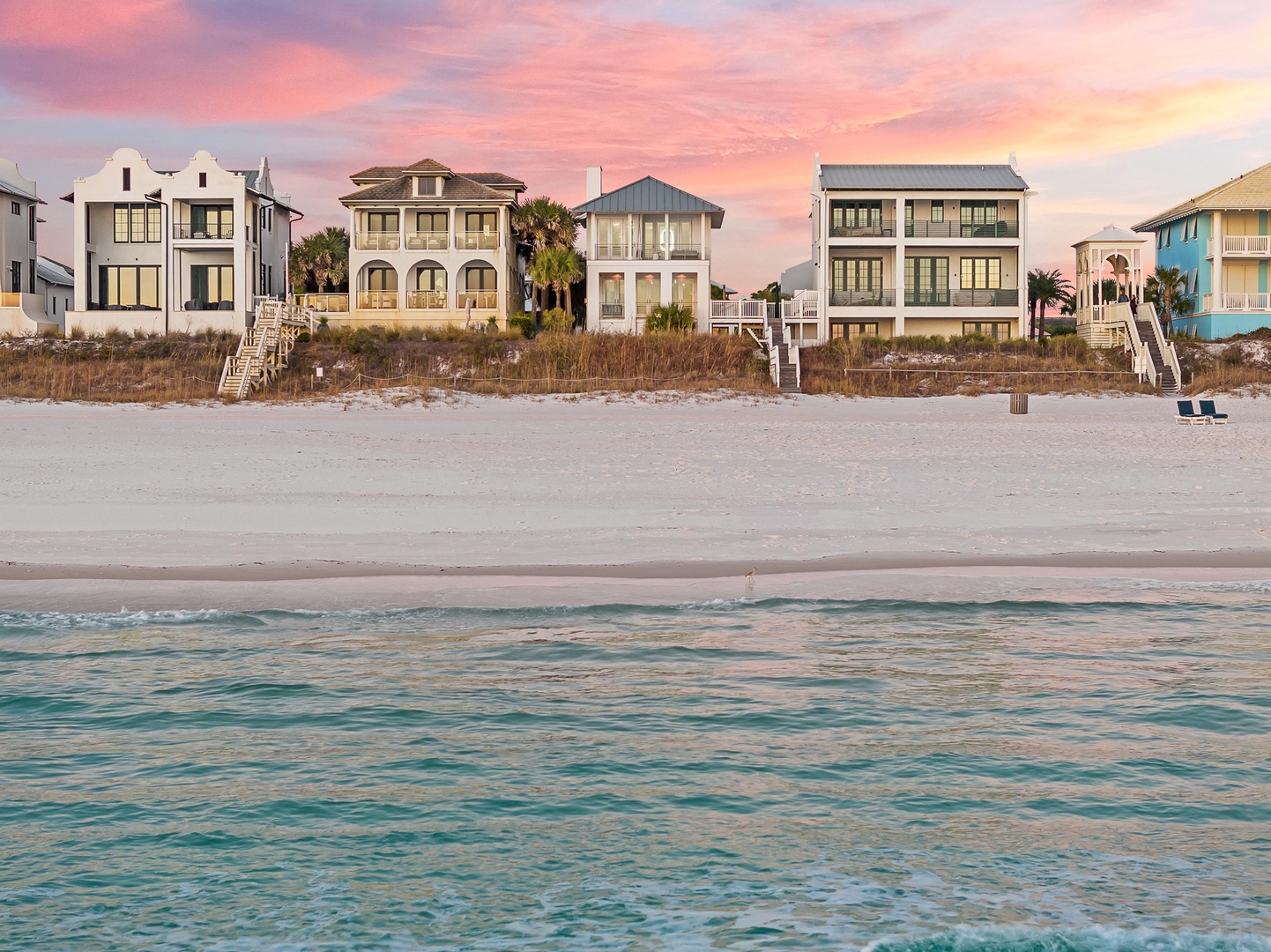 Stunning beachfront properties line pristine sand under a dramatic sunset sky, offering direct beach access and coastal charm.
