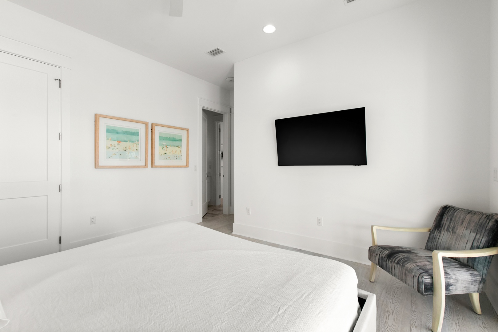 Drift off in this serene bedroom with a plush bed, wall-mounted TV, and modern furnishings. The soft white palette and natural light create a calming retreat for your stay.
