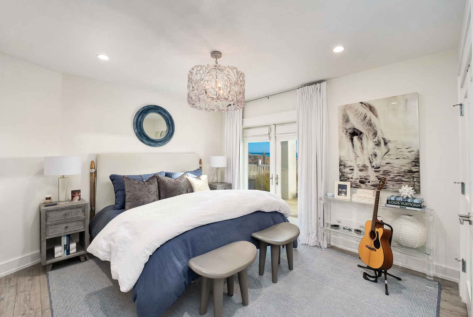 Unwind in your serene bedroom retreat with plush bedding, elegant chandelier lighting, and coastal-inspired decor—your peaceful ocean view awaits just beyond the balcony doors.