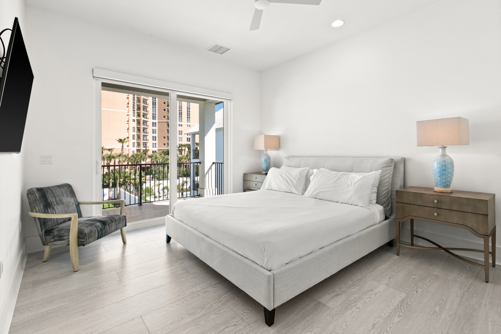 Unwind in your bright, serene bedroom with crisp linens and calming coastal hues. Step through the glass doors to your private balcony, where palm trees and warm sunshine invite you to relax.