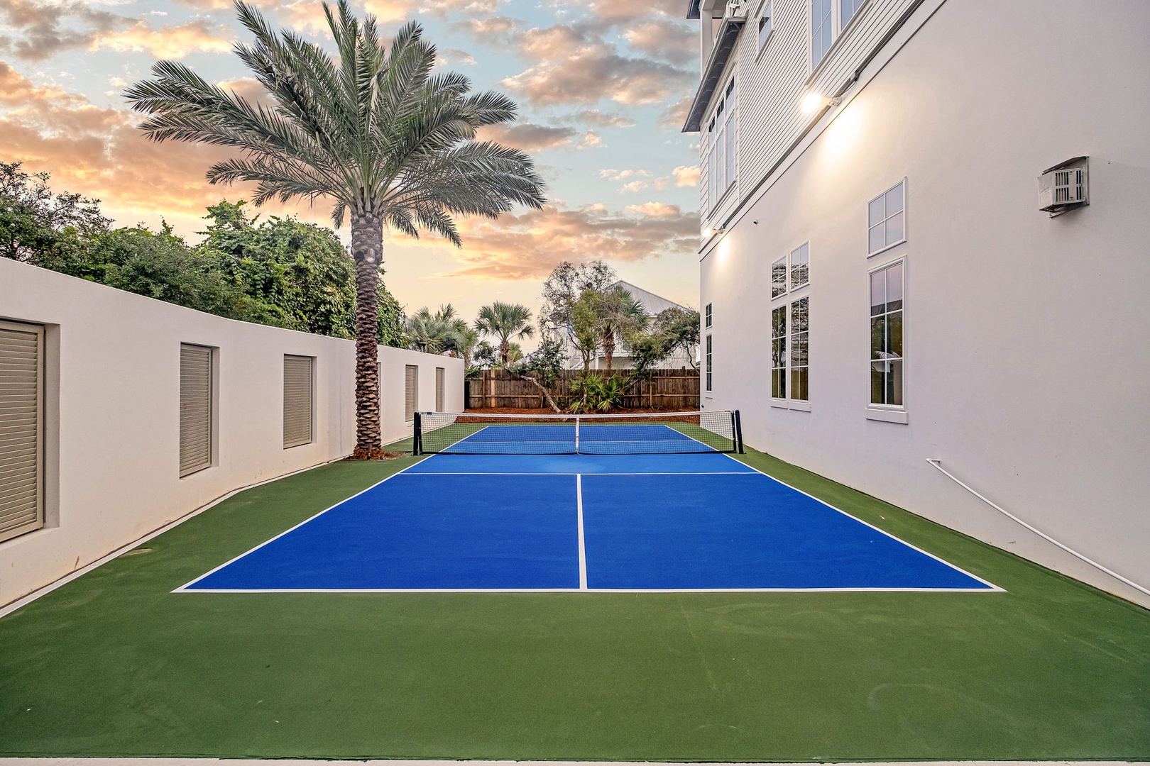Private tennis court framed by tropical palms and a dramatic sunset sky, perfect for friendly matches during your stay.