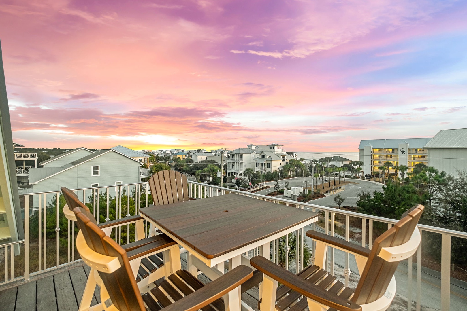 Unwind on your private balcony with teak dining furniture as breathtaking sunset colors paint the sky above the coastal neighborhood below.