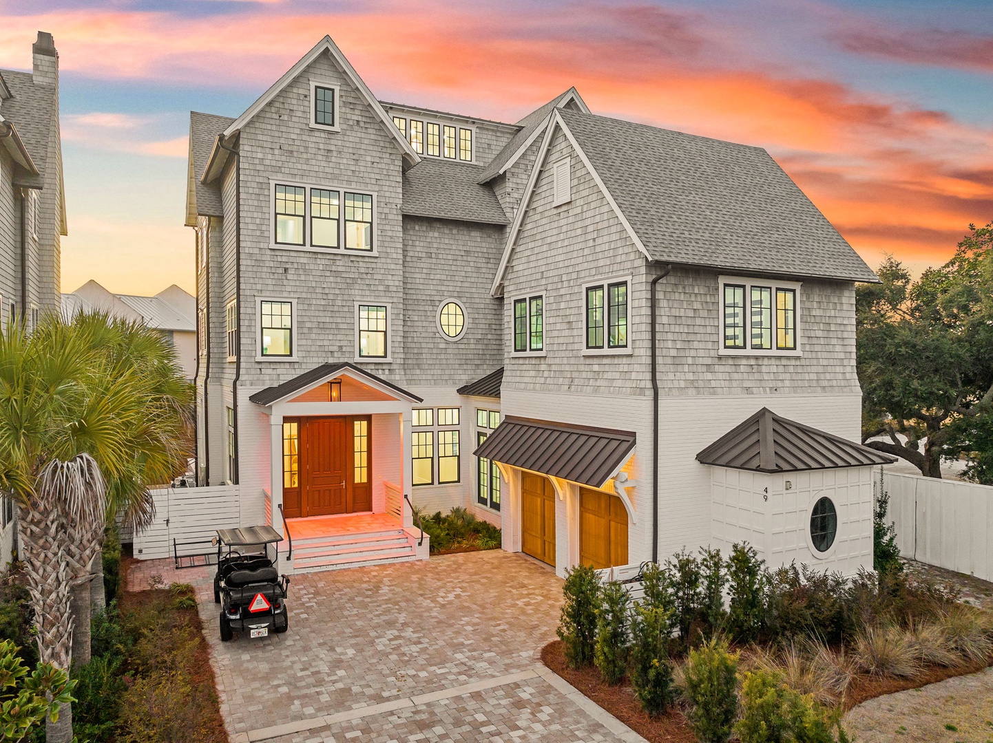 Stunning coastal home with elegant shingle siding and warm lighting awaits your arrival at sunset.