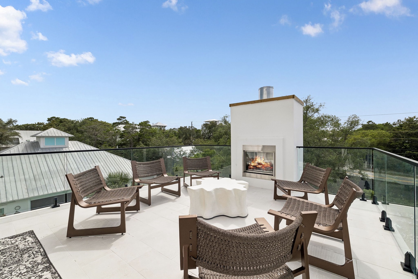 A spacious rooftop terrace with contemporary outdoor fireplace creates the perfect setting for coastal evenings under open skies, surrounded by treetops and ocean breezes.