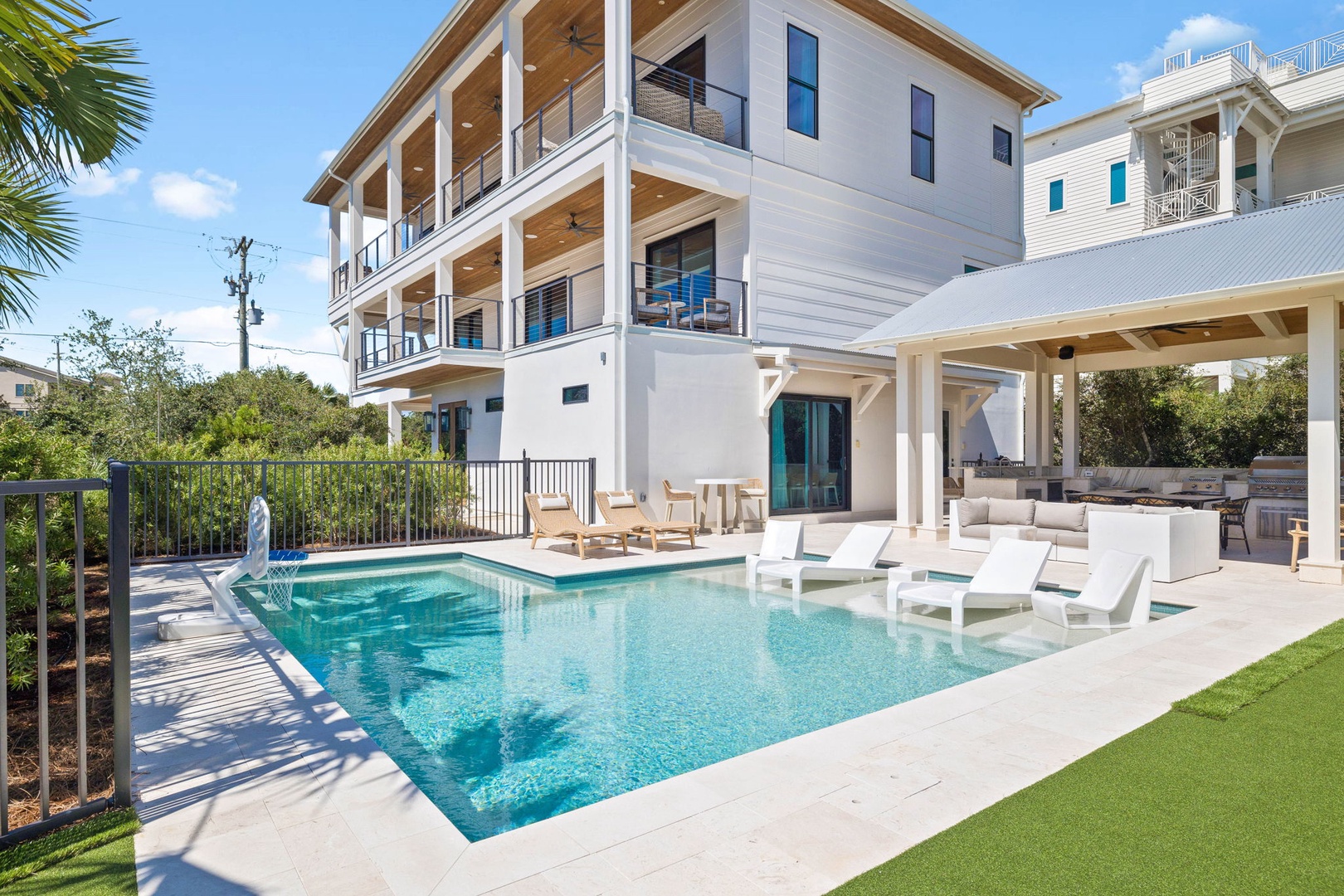 A modern three-story coastal retreat featuring a private pool surrounded by lounge seating and covered outdoor living space. The multi-level balconies and contemporary architecture create an inviting atmosphere for relaxation.