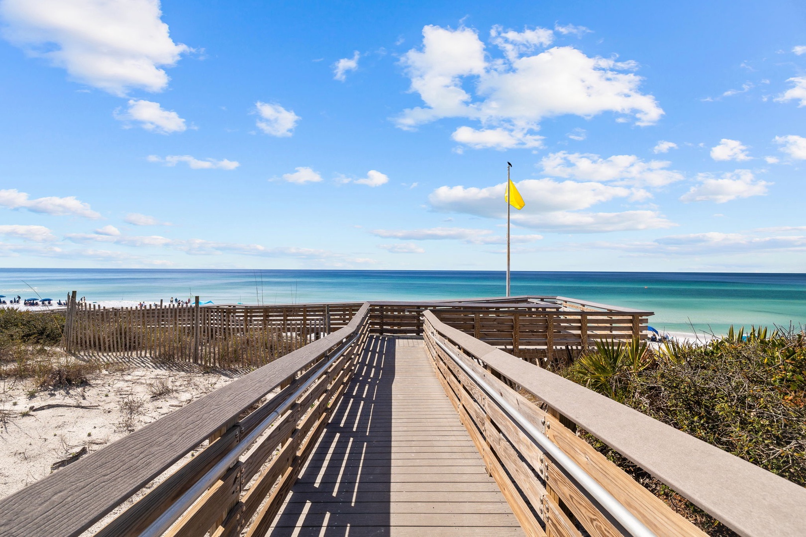 Wooden boardwalk leads directly to pristine white sand beach and crystal-clear turquoise waters under expansive blue skies.