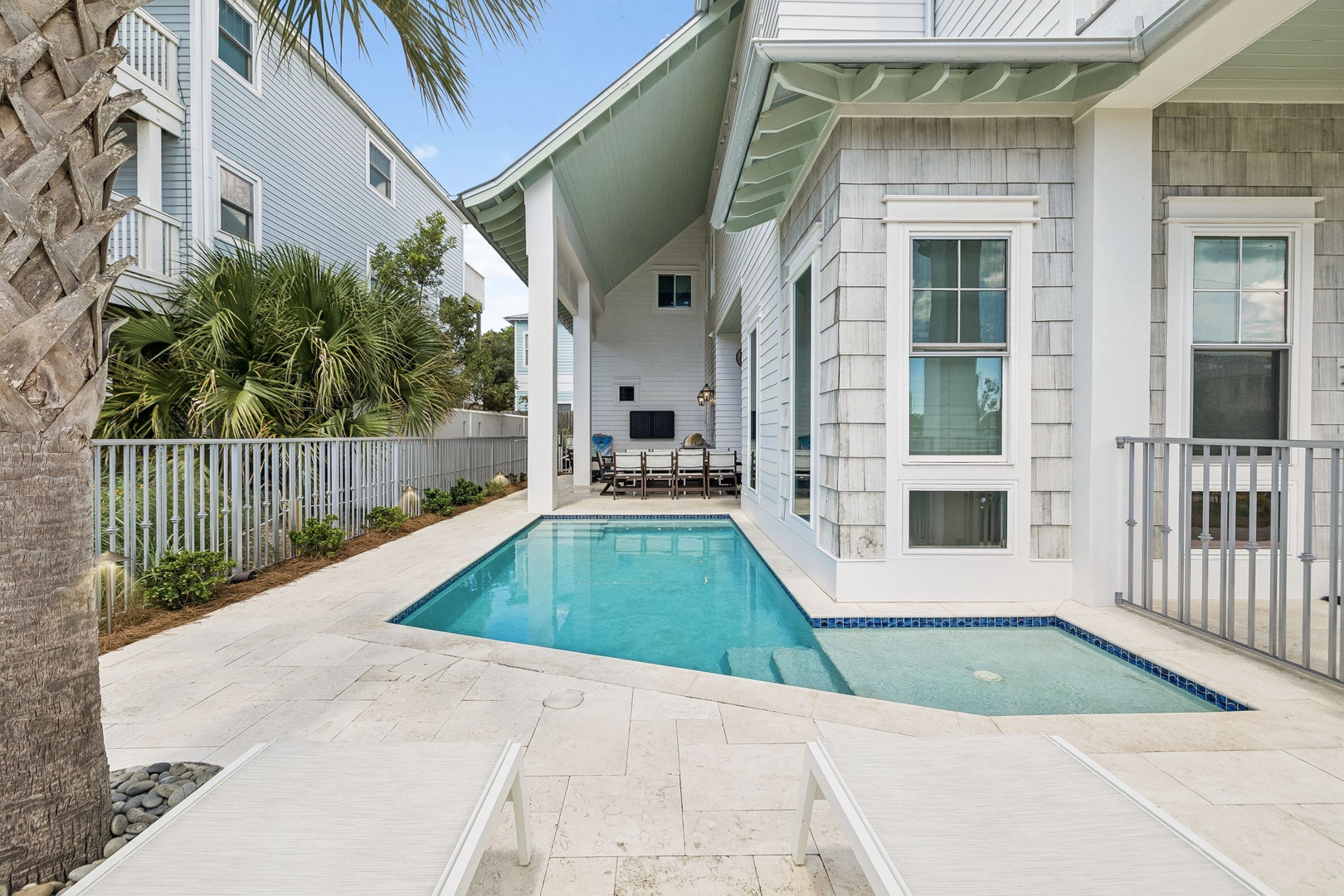 This coastal-inspired property features a private swimming pool nestled between coastal homes, with palm trees dotting the landscaped backyard. The property offers a relaxed outdoor retreat perfect for sunny days.