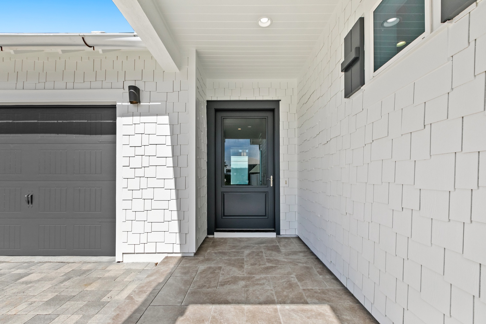 Bright white shingle siding and a sleek front door with glass detail mark the welcoming entrance to this coastal property, complete with garage access.