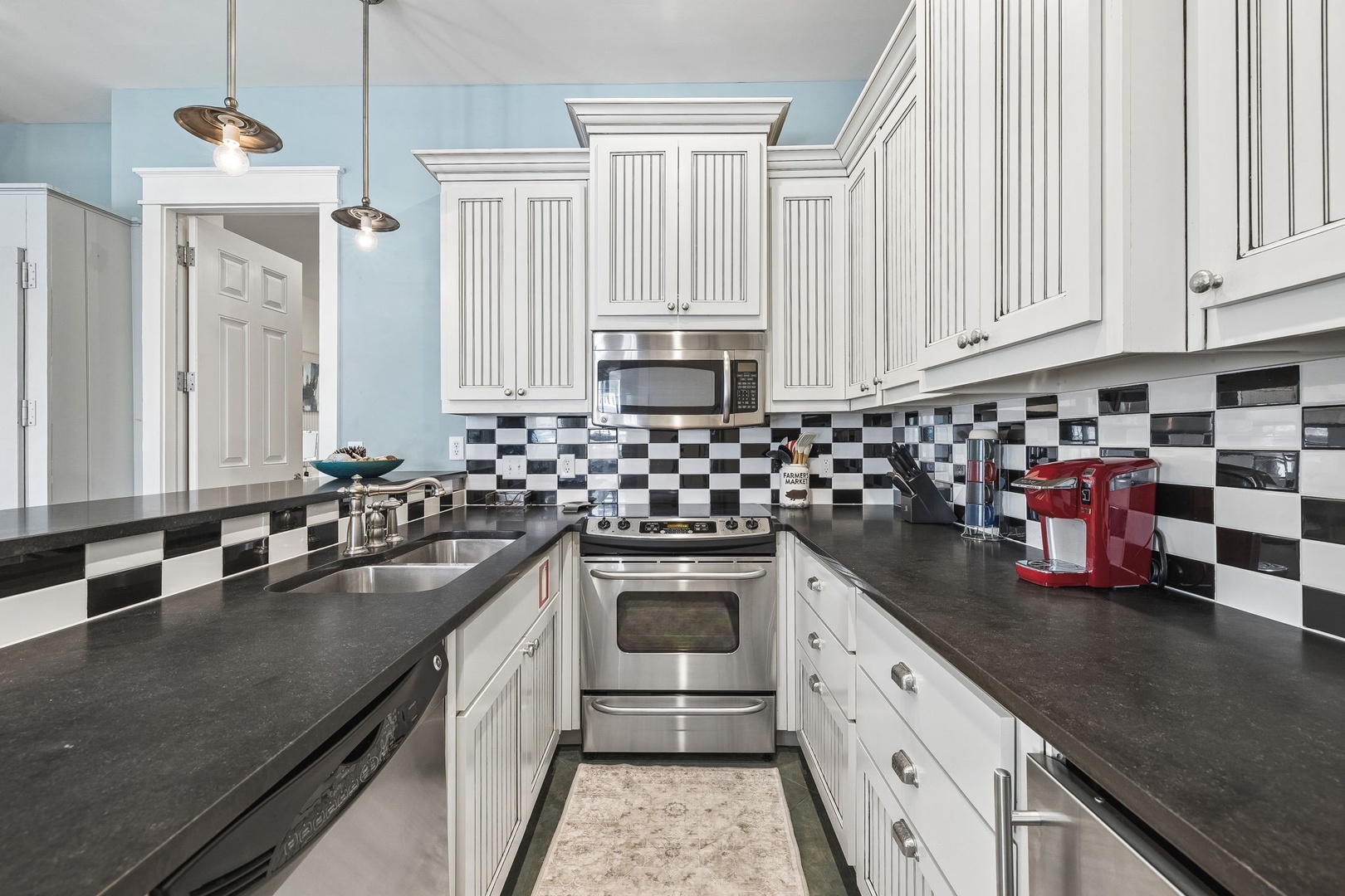 Prepare your favorite meals in this bright, fully-equipped kitchen featuring classic white cabinetry, modern stainless steel appliances, and eye-catching checkerboard tile backsplash—your perfect culinary retreat.