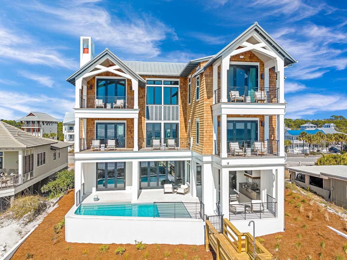 Stunning three-story beach house featuring cedar shingle siding, multiple balconies, and a private pool surrounded by coastal landscape.
