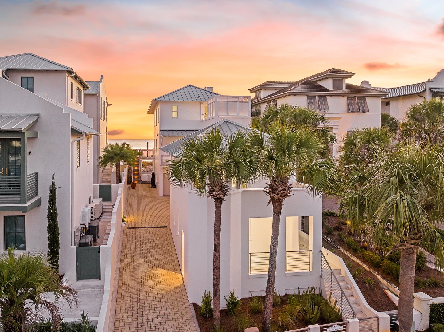 Modern coastal architecture frames a stunning sunset in this peaceful beachside community, where palm trees sway against painted evening skies.