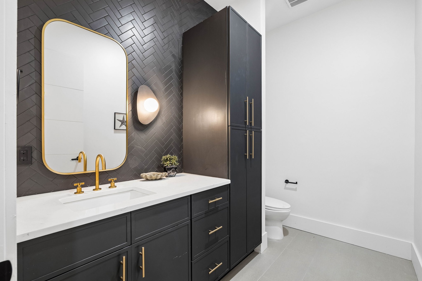 Freshen up in your sophisticated bathroom featuring luxe herringbone tile, elegant brass fixtures, and a pristine marble countertop that brings a boutique hotel vibe to your morning routine.