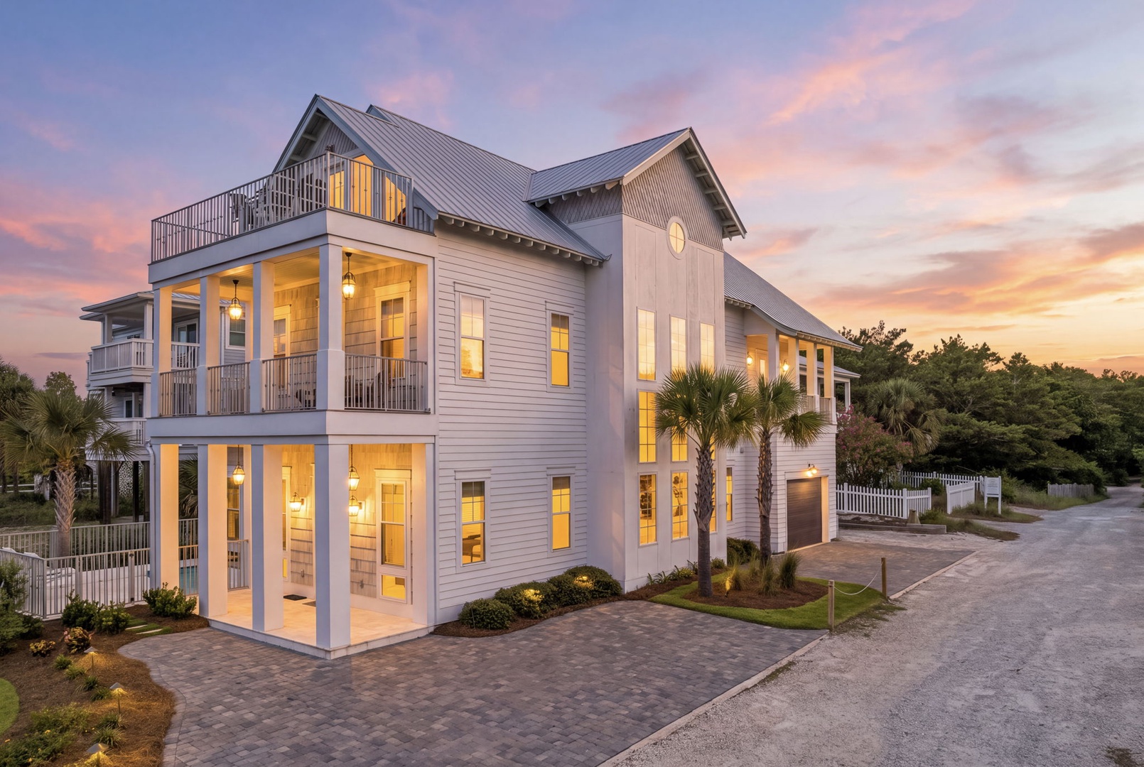 A stunning modern beach home with soaring windows and spacious balconies, framed by palms and painted in the soft glow of a breathtaking coastal sunset.