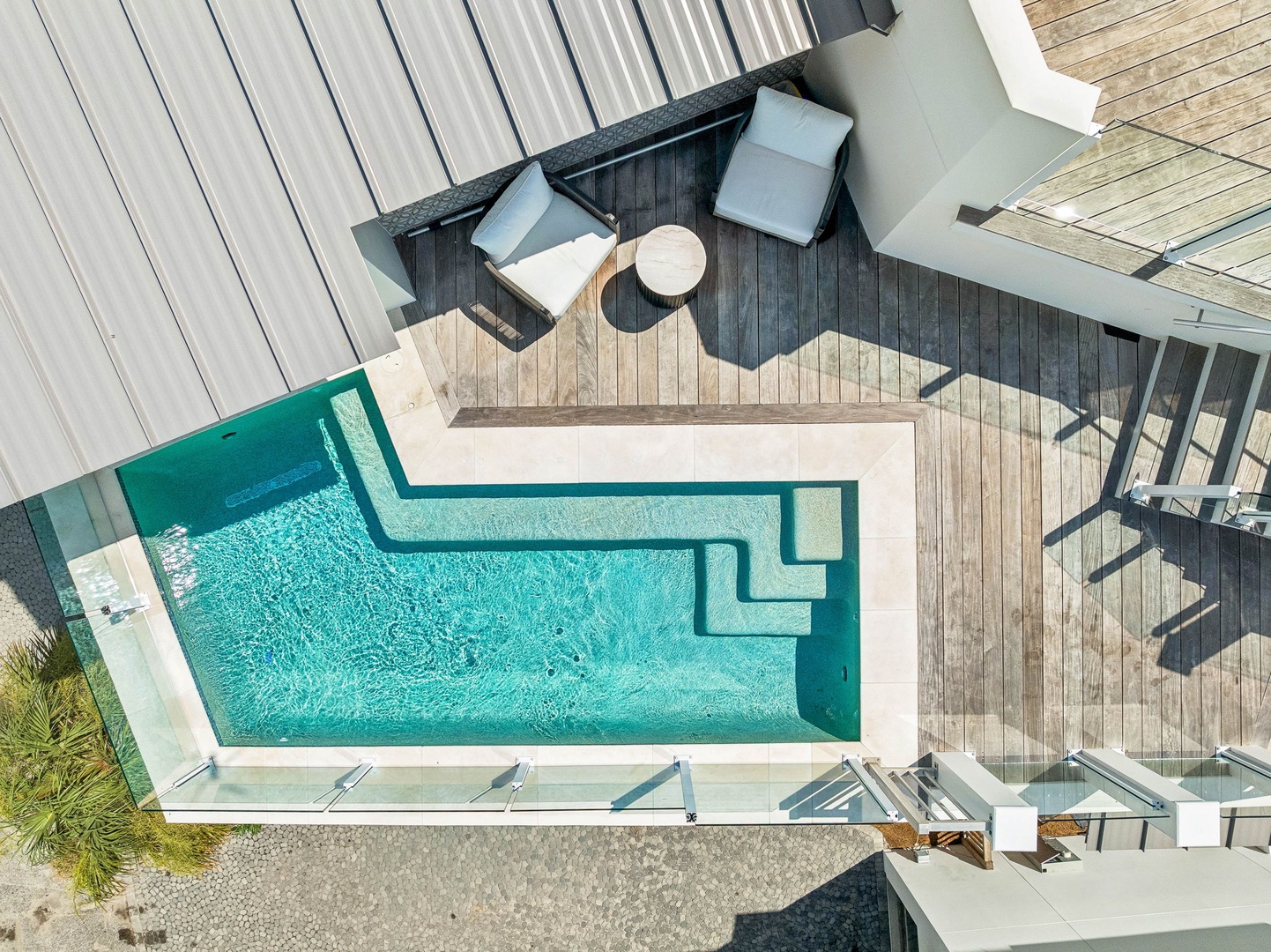 Aerial view of contemporary outdoor living area featuring an inviting turquoise pool bordered by natural wood decking, modern furniture, and glass barriers—part of the property's surrounding resort-style grounds.