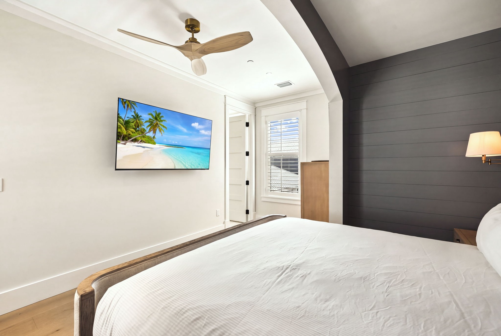 Drift off to sleep beneath a gentle ceiling fan in your serene bedroom, where coastal modern style meets comfort with fresh white walls and a striking accent wall.