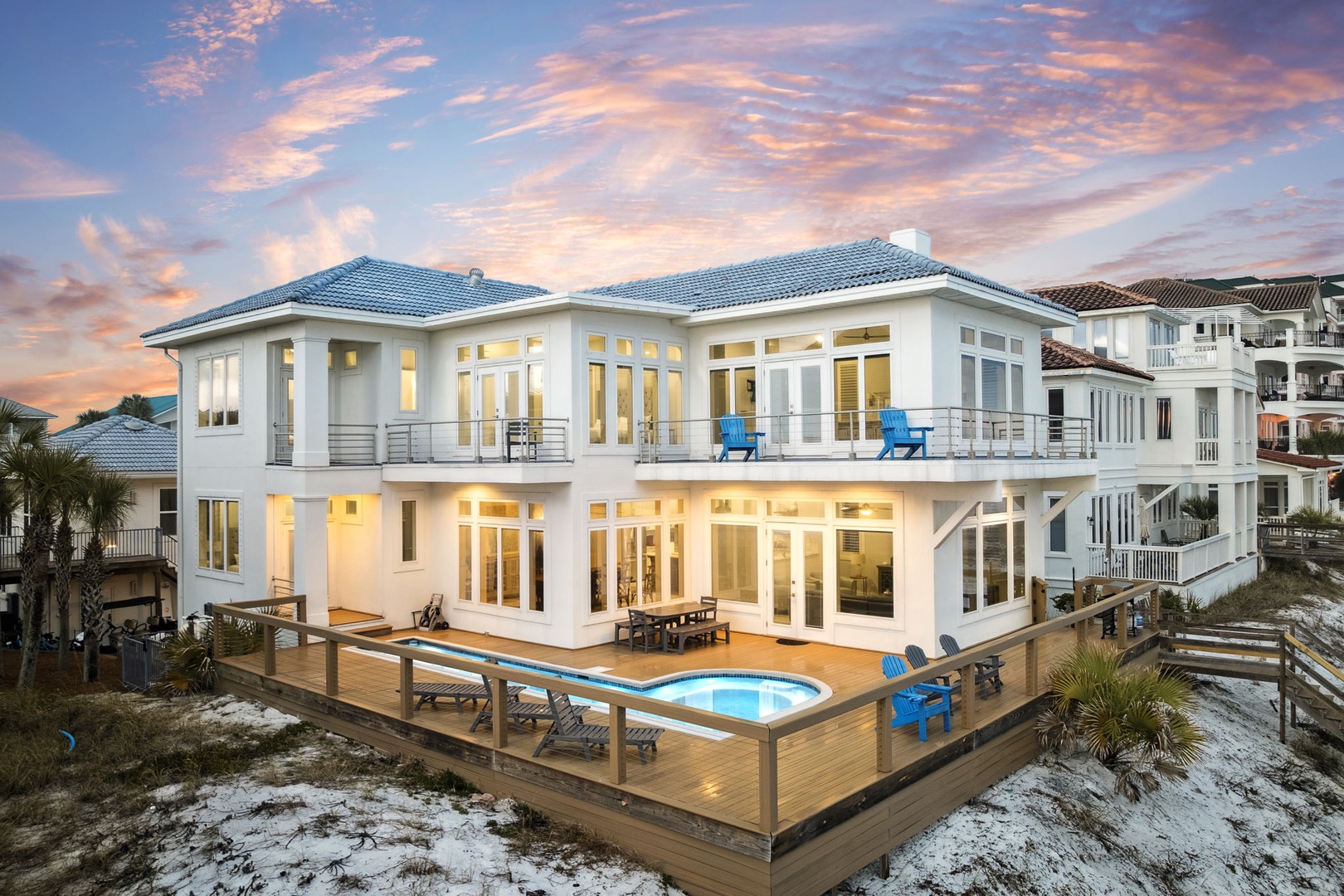 Stunning beachfront villa featuring expansive deck, pool, and dramatic sunset views across pristine sandy shores.